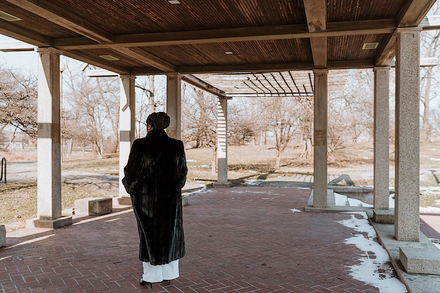 Bride wearing a coat standing underneath wooden overhang
