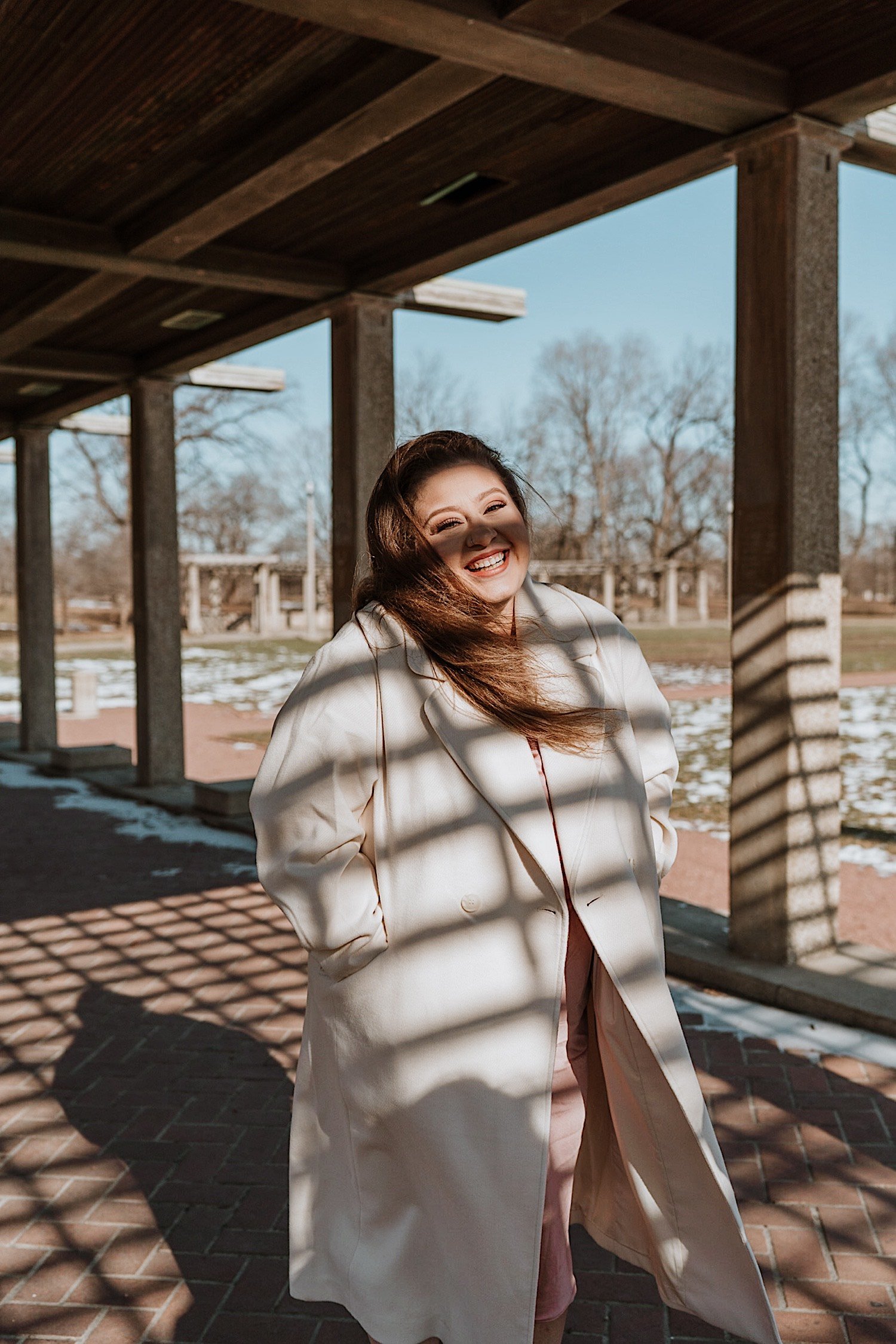Bride wearing a coat laughs underneath wooden overhang