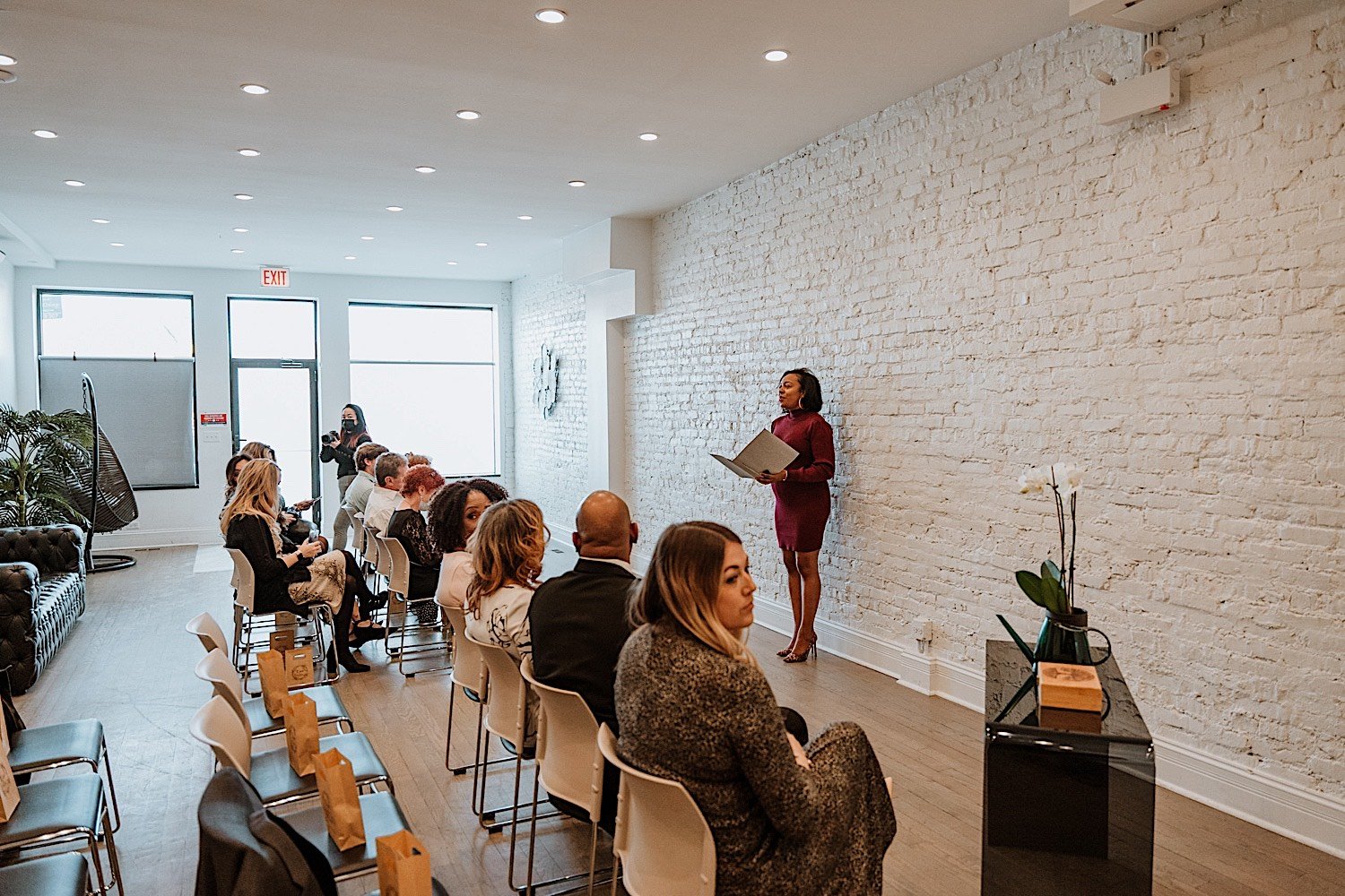 Woman standing in front of seated wedding guests introducing the soon to be married couple