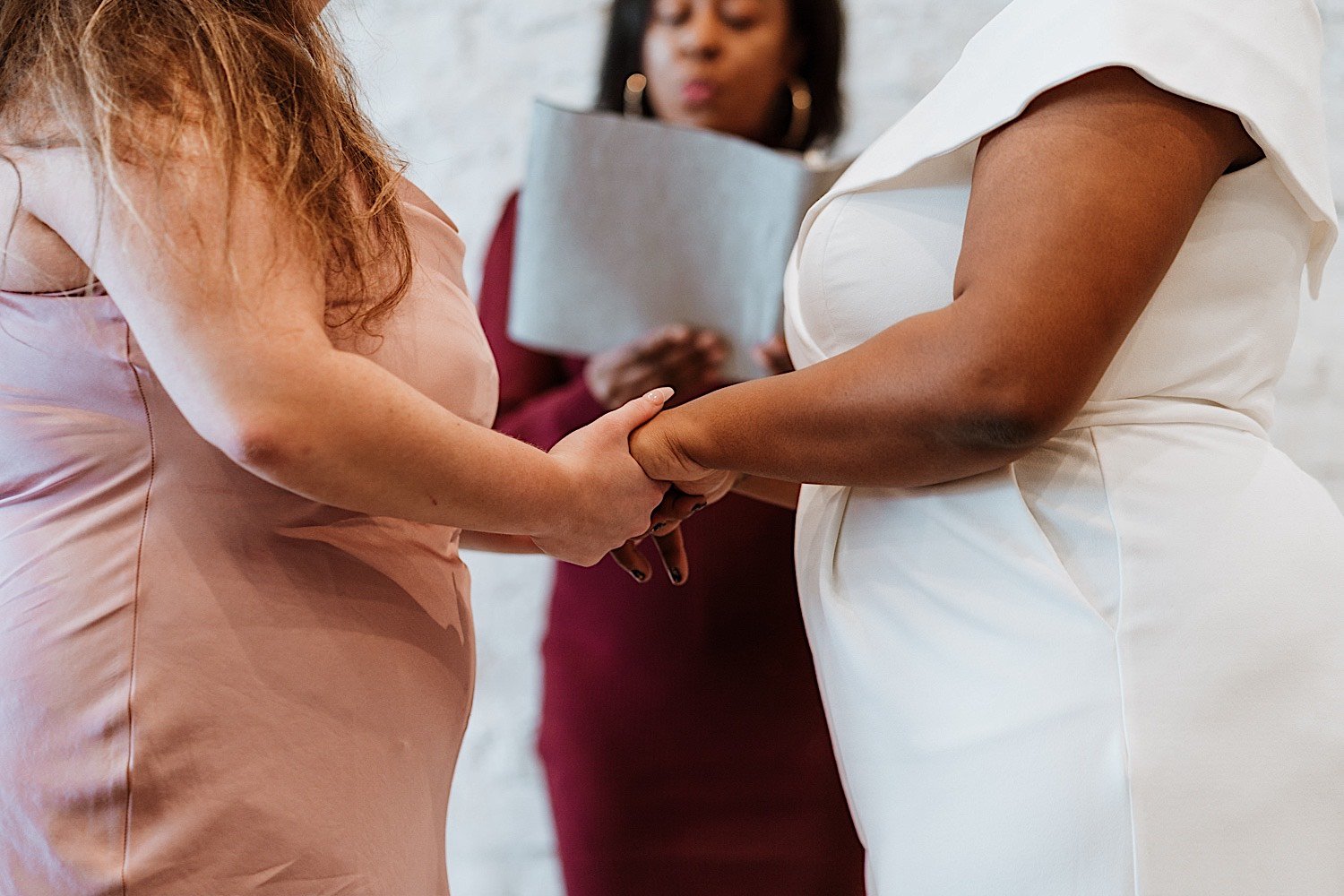 Brides hold hands during their wedding ceremony