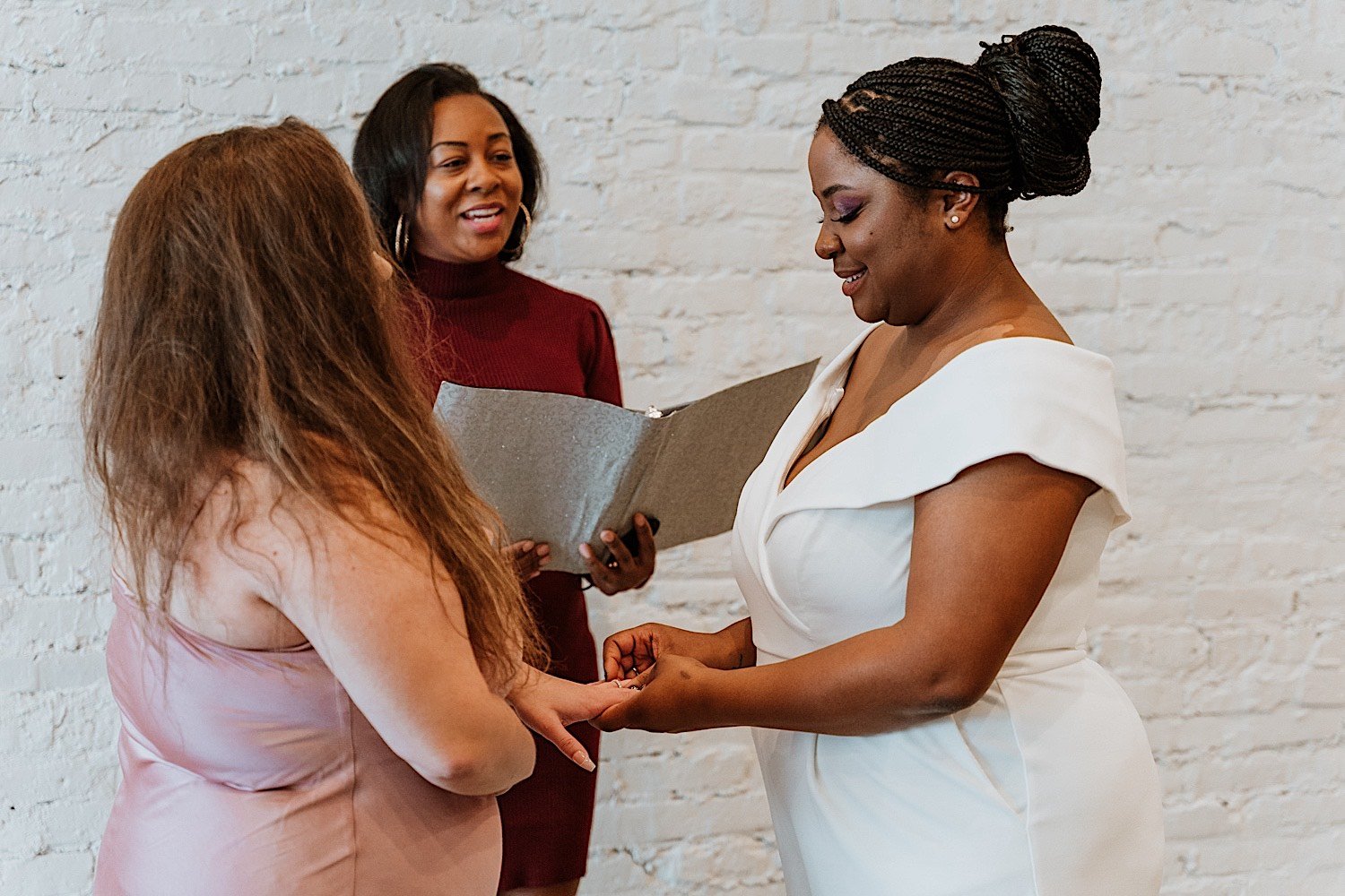 Couple exchanges rings in front of white wall during wedding ceremony