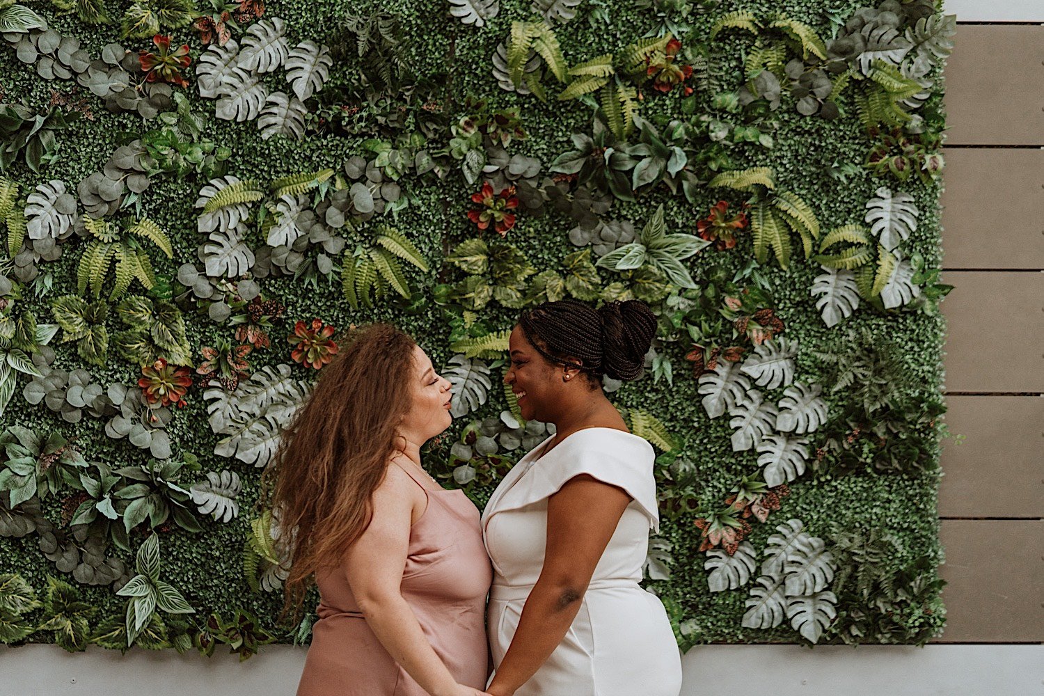 Brides look at one another in front of art display of leaves