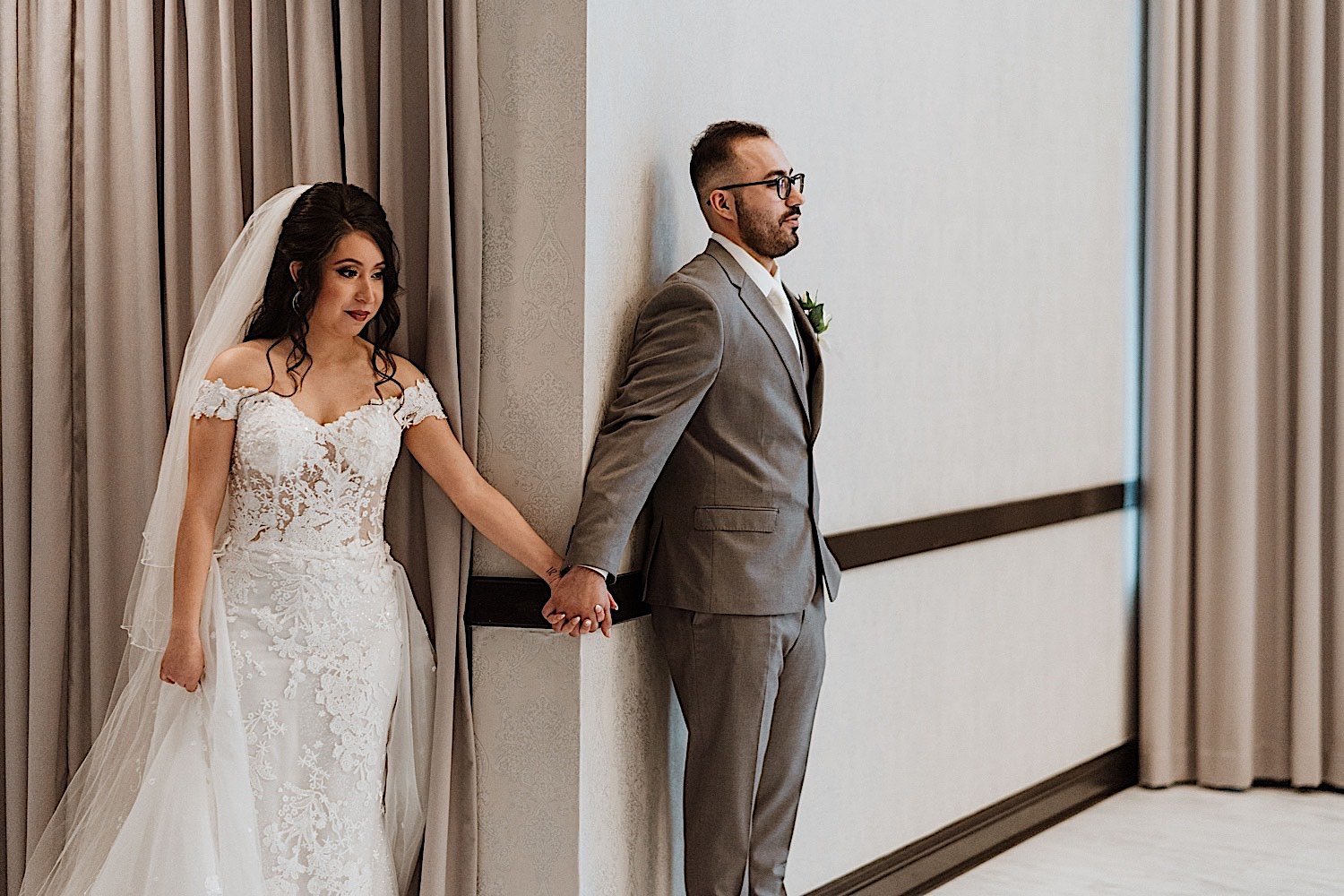Bride and groom holding hands around a corner without looking at eachother
