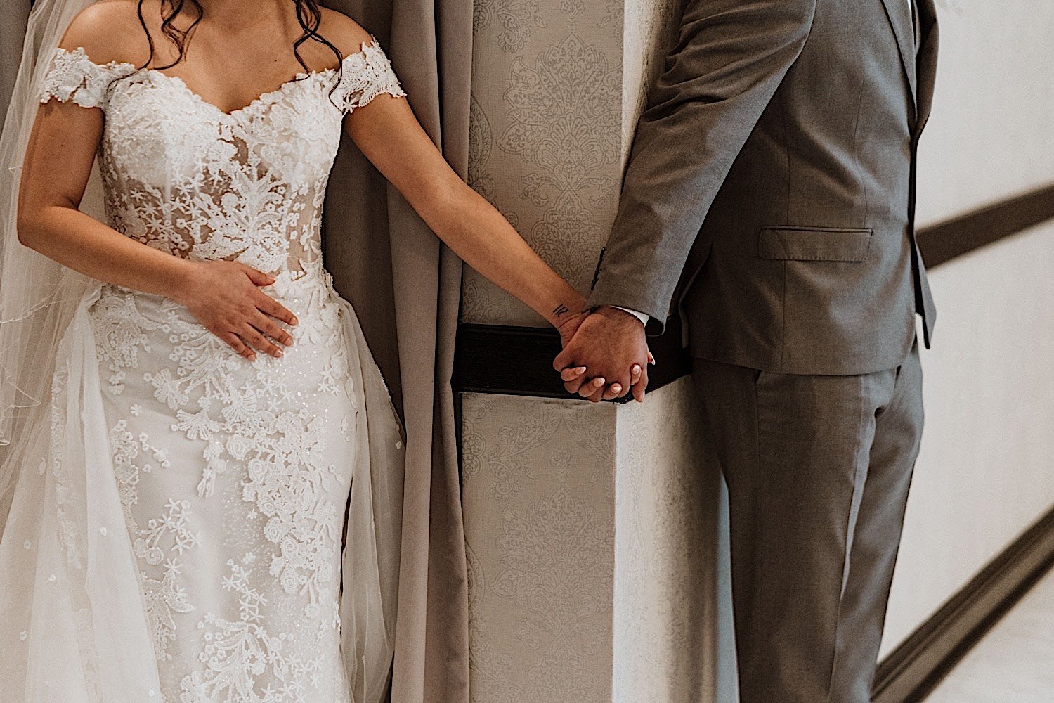 Closeup of bride and groom holding hands around a corner