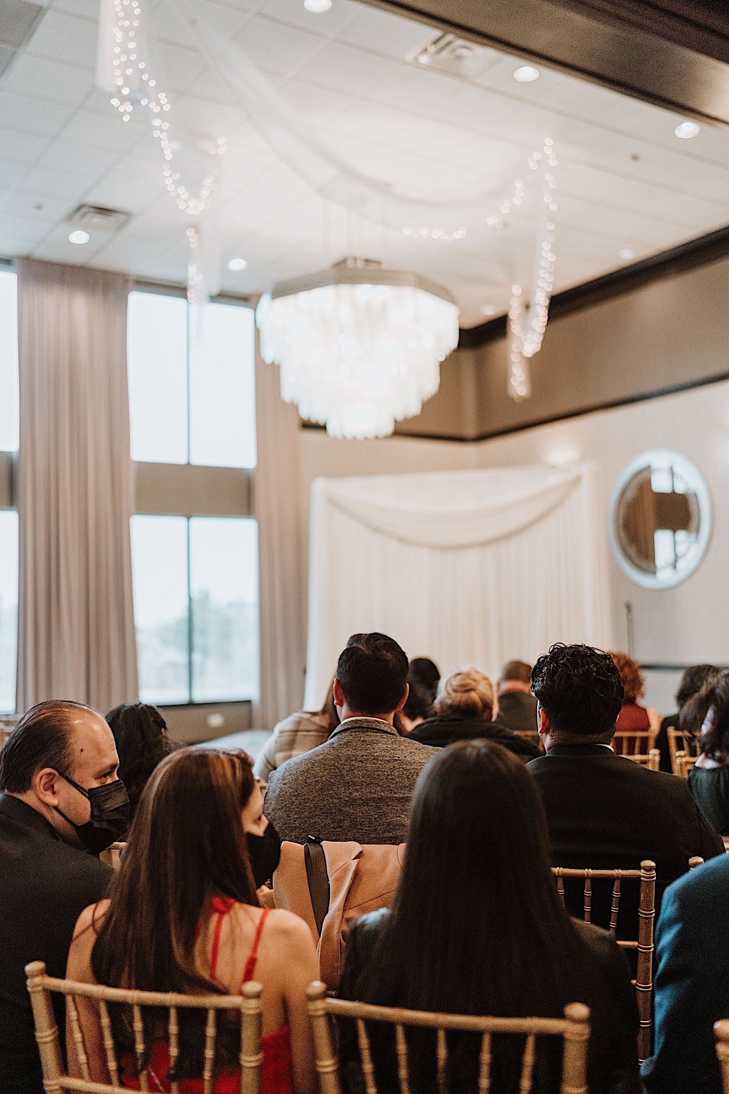 Guests seated in a ballroom for a wedding with a large glass chandelier overhead