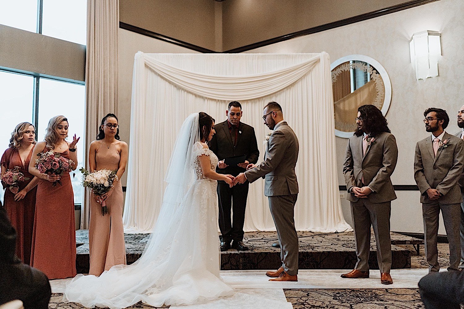 Bride and groom holding hands during their Chicagoland ballroom wedding with wedding party standing on either side of them