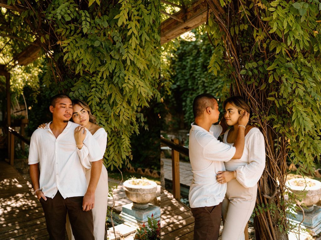 An engaged couple stands close together while holding one another standing outside underneath a pergola covered in leaves at a Chicago wedding venue