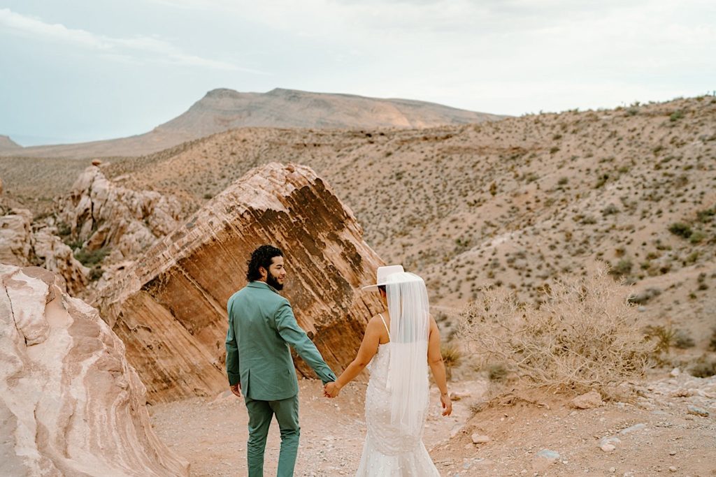 A bride and groom hold hands during their elopement standing in front of red rocks in Las Vegas Nevada.