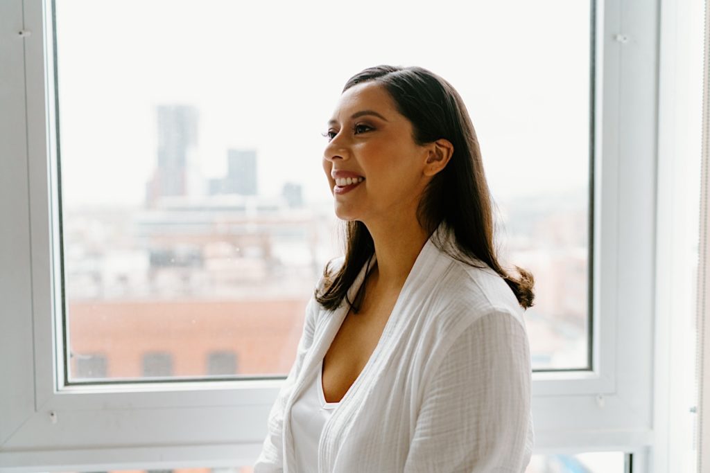 The bride smiles at her bridal party in front of a window overlooking the city of Chicago.