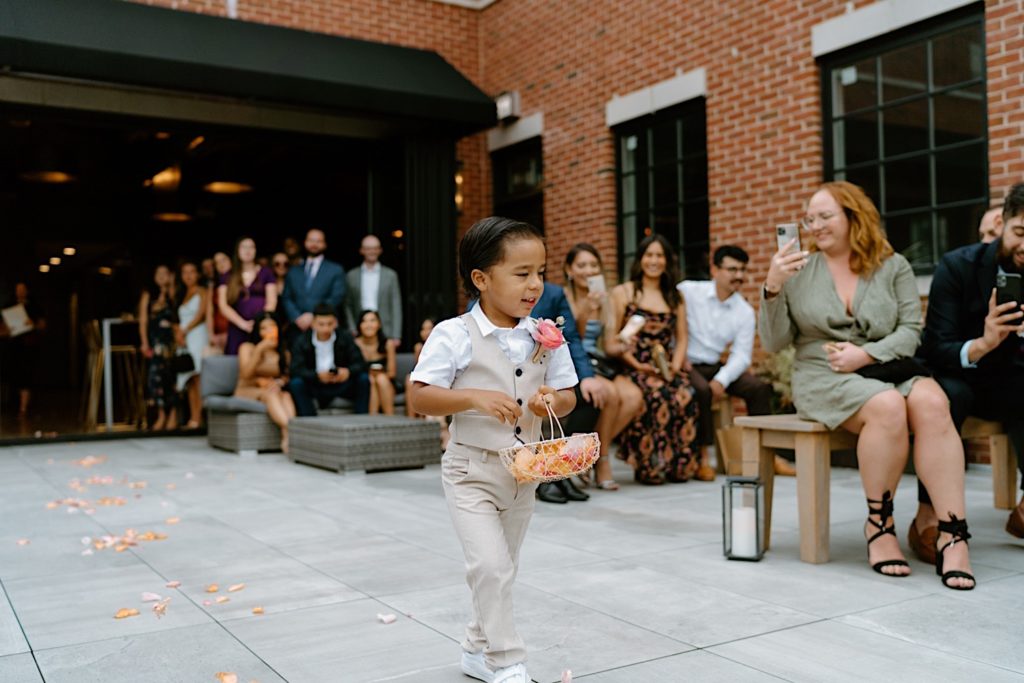 The flower boy walking down the aisle spreading pink and orange flower petals up to the ceremony on the rooftop of Loft Lucia.