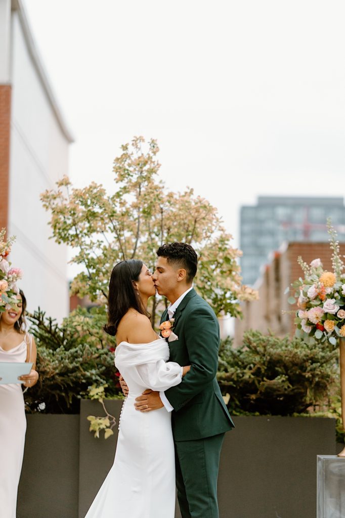 The bride and groom kiss at the end of their ceremony at Loft Lucia surrounded by their loved ones and flowers