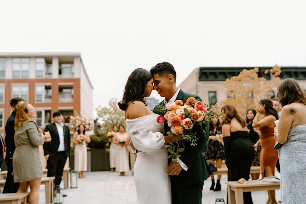 The bride and groom hold hands leaving their ceremony space on a rooftop at Loft Lucia in Chicago.