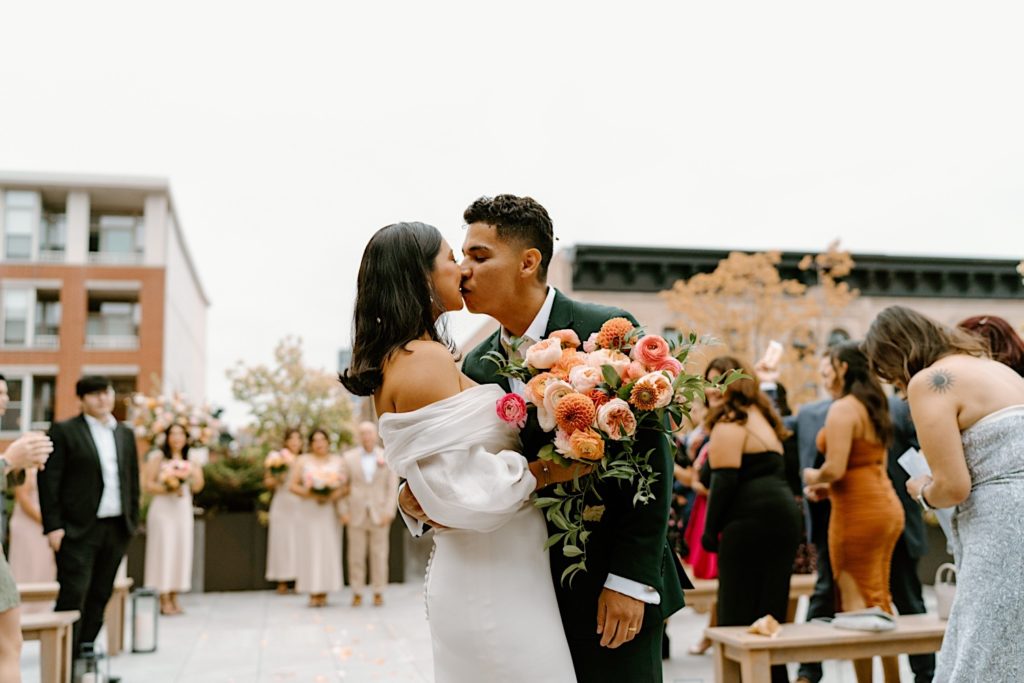 The bride and groom kiss on the way out of leaving their ceremony space on a rooftop at Loft Lucia in Chicago.