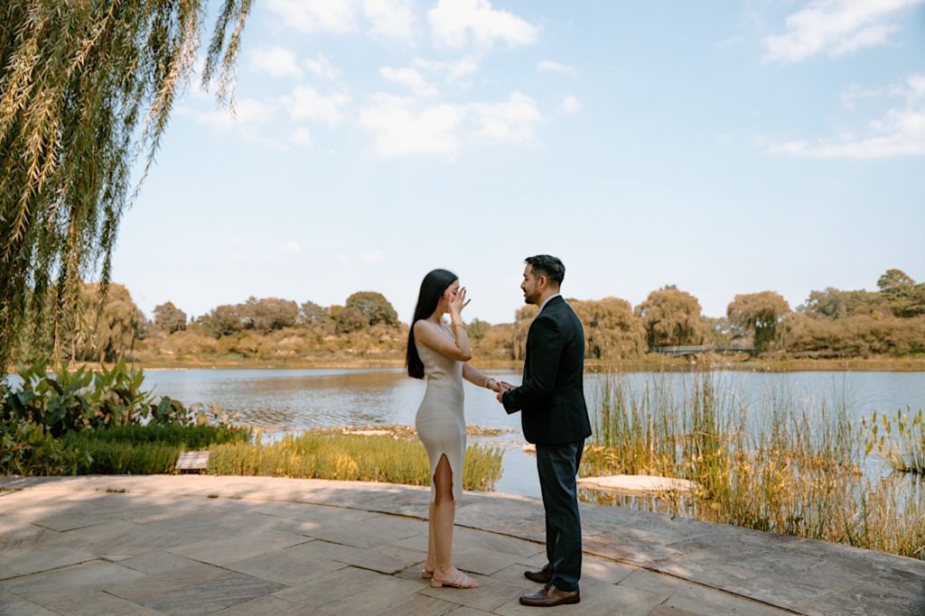 A couple holds hands overlooking a pond on a beautiful clear sky day in the Chicago Botanic Gardens