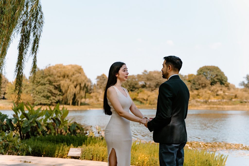 A couple holds hands facing one another overlooking a pond on a beautiful clear sky day in the Chicago Botanic Gardens