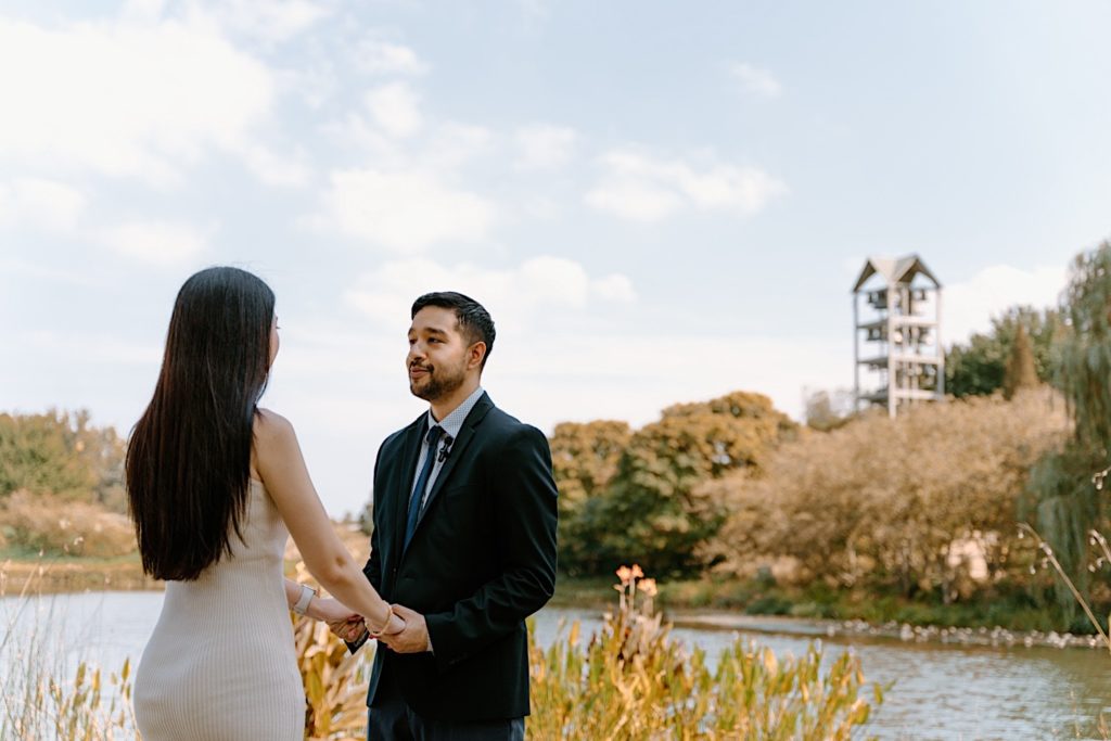 A couple holds hands facing one another overlooking a pond on a beautiful clear sky day in the Chicago Botanic Gardens