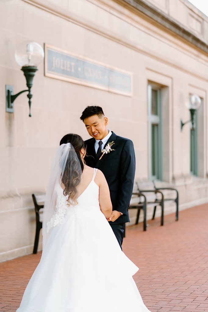 A bride and groom stand holding one another during their first look standing underneath the overhand at Joliet's Union Station.