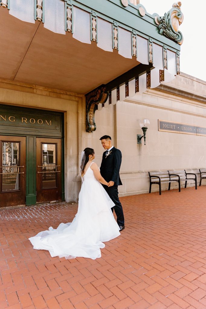 A bride and groom stand holding one another during their first look standing underneath the overhand at Joliet's Union Station.