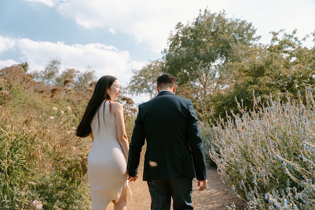 Fiancé's hold hands walking over a bridge at the Chicago Botanic Gardens.
