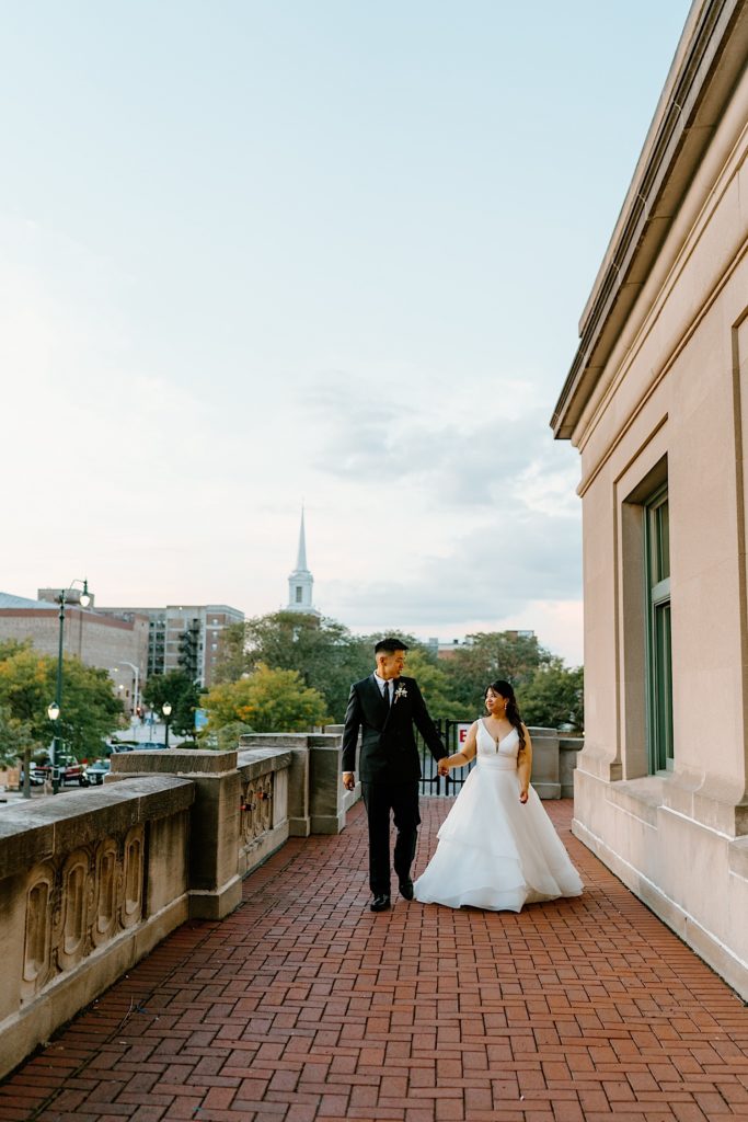A bride and groom take wedding portraits together on the balcony at Joliet Union Station walking together towards the camera.