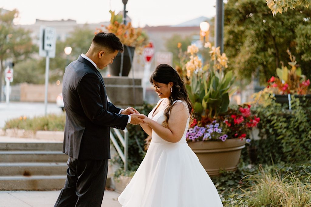 A bride and groom stand in the gardens outside of Joliet Union Station during their wedding portraits holding hands.