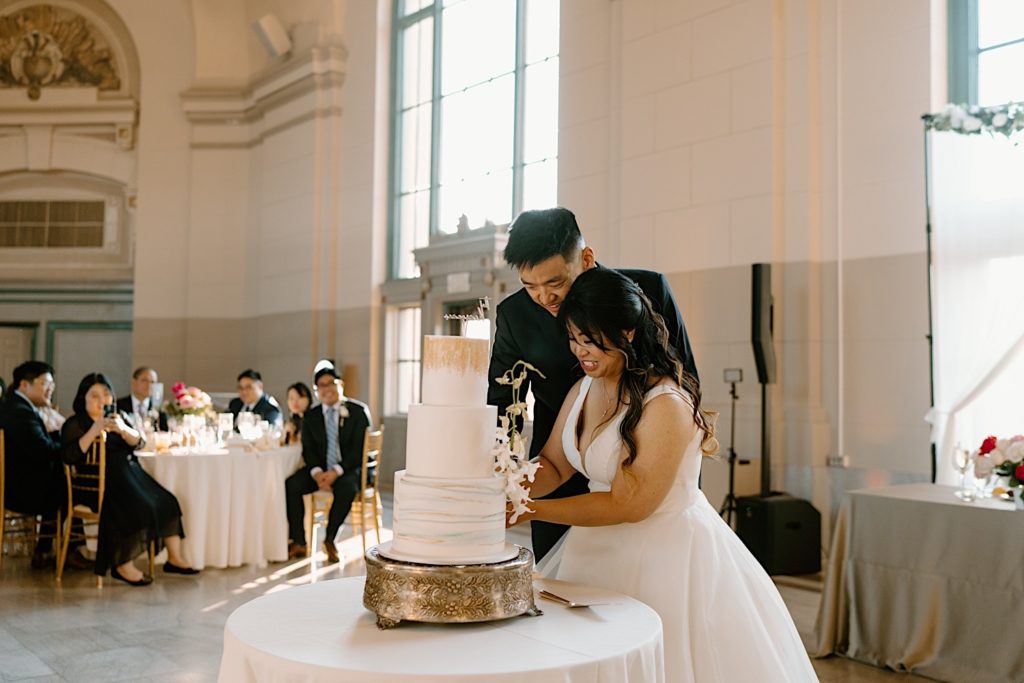 The bride and groom go to cut their cake at the reception at Joliet Union Station celebrating with their guests.