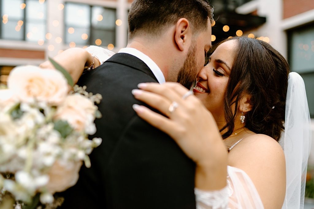 A bride and groom snuggle in close almost kissing surrounded by lights during their wedding reception in Chicago.