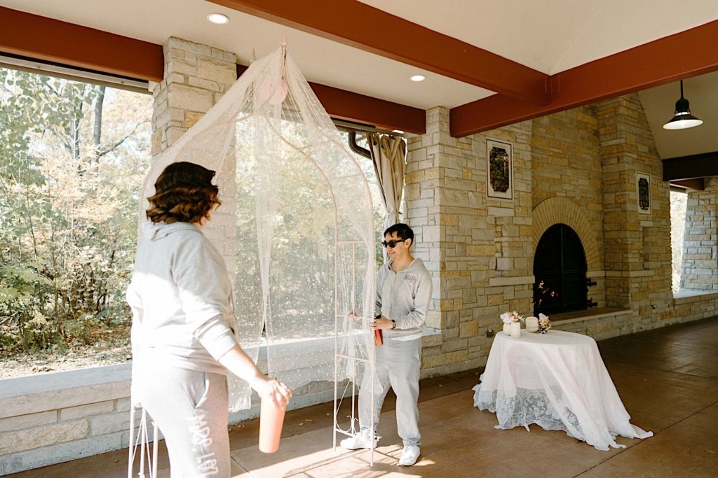 A bride and groom setting up their ceremony space in matching sweatpants at the Grove Redfield Estate.
