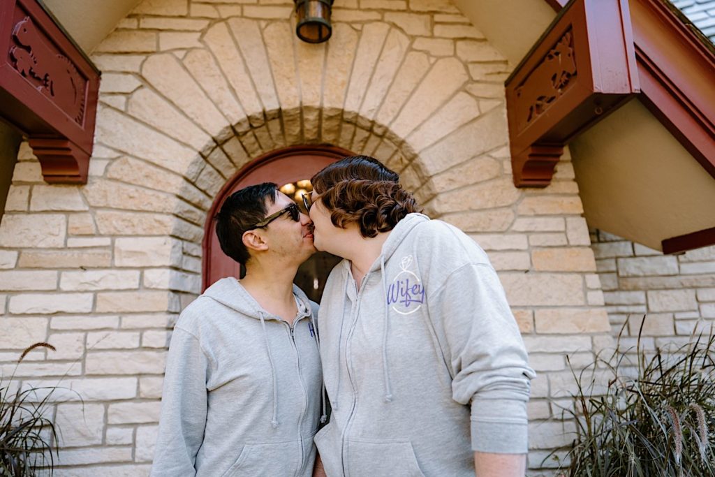 A bride and groom stand kissing in matching sweat suits outside of the Grove Redfield Estate.