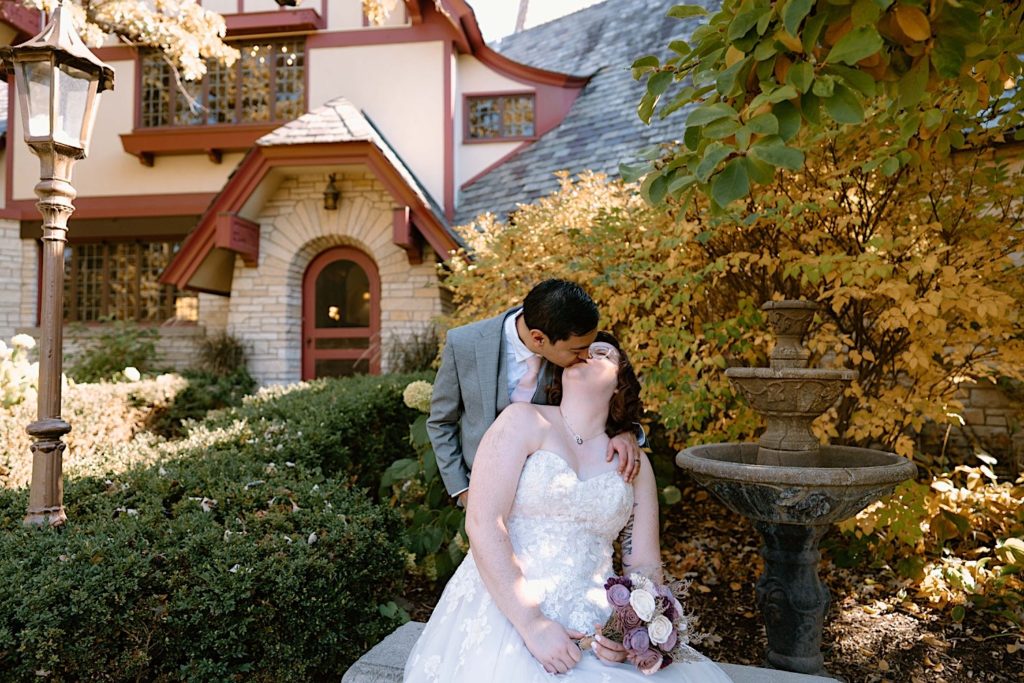 A bride and groom sit in front of the Grove Redfield Estate in the fall after their elopement ceremony.