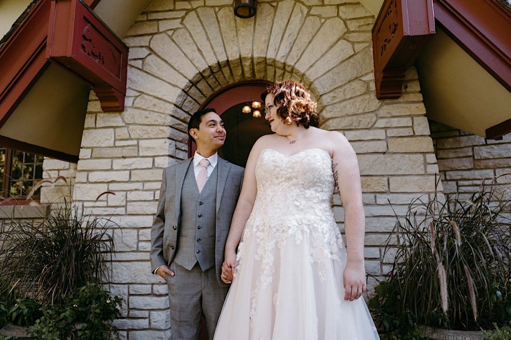 A bride and groom stand outside holding hands and looking at one another after their elopement at the Grove Redfield Estate