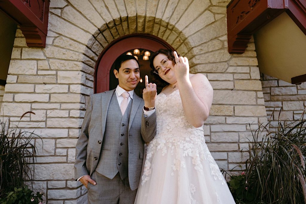 A bride and groom hold up their wedding ring fingers showing off their wedding rings after their elopement at the Grove Redfield Estate