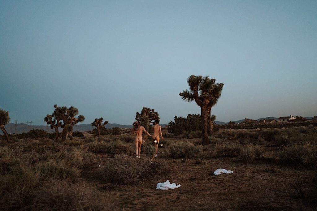 A bride and groom walk nude across the desert after their evening elopement in Moab Utah.