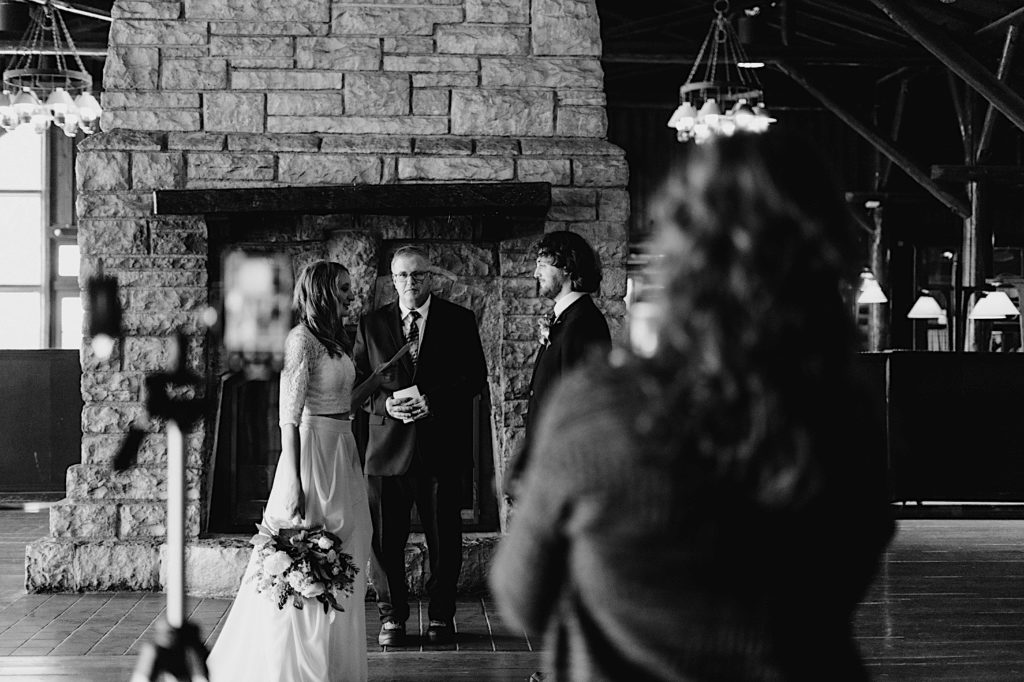 A bride and groom stand during their wedding ceremony at a cabin in Starved Rock National Park while their guests watch via zoom.