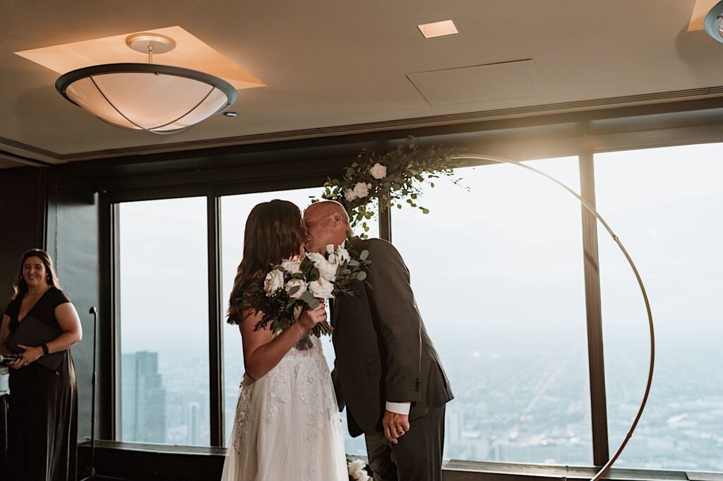 A bride and groom kiss during their wedding ceremony overlooking the city of Chicago in the Signature Room on the 95th floor.