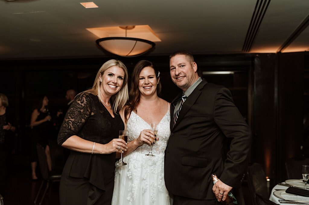 A bride stands with guests smiling at the camera holding glasses of champagne.