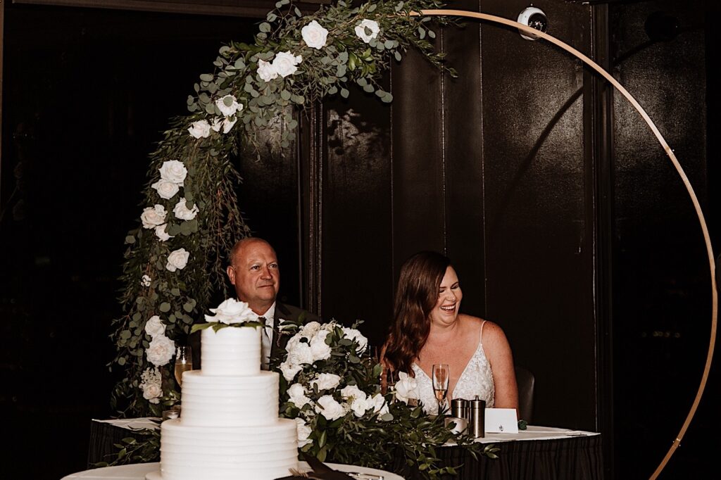 A bride and groom smile and laugh during a speech at their wedding on the 95th floor Signature Room