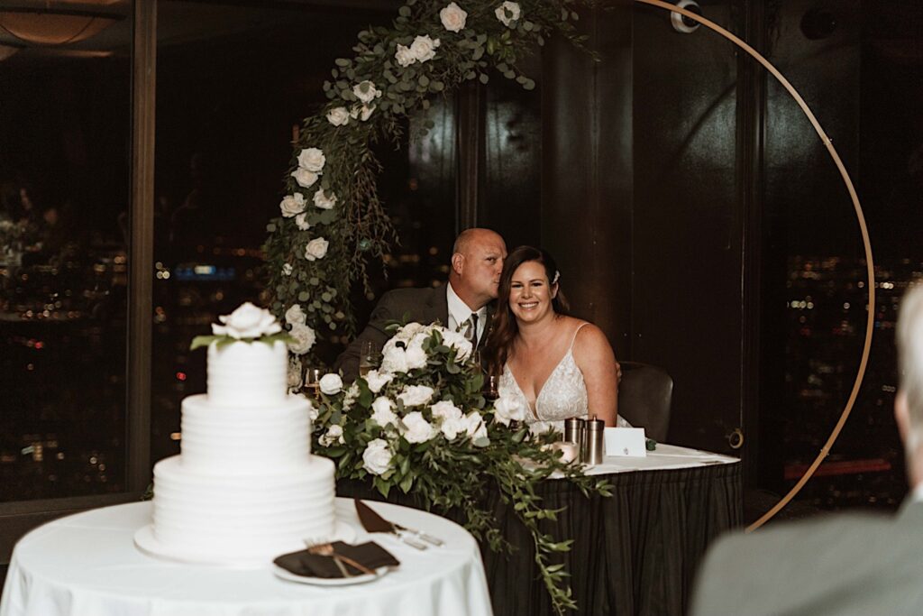 A bride and groom kiss during their dinner at their wedding reception on the 95th Floor in the John Hancock Building.