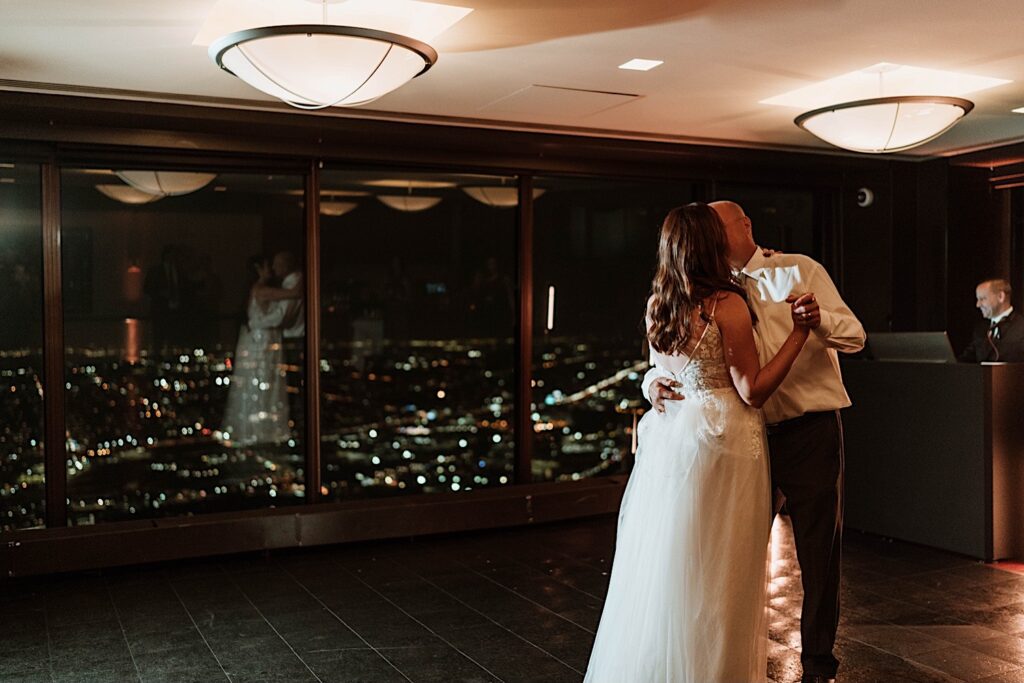 A bride and groom have their first dance overlooking the Chicago night time sky.