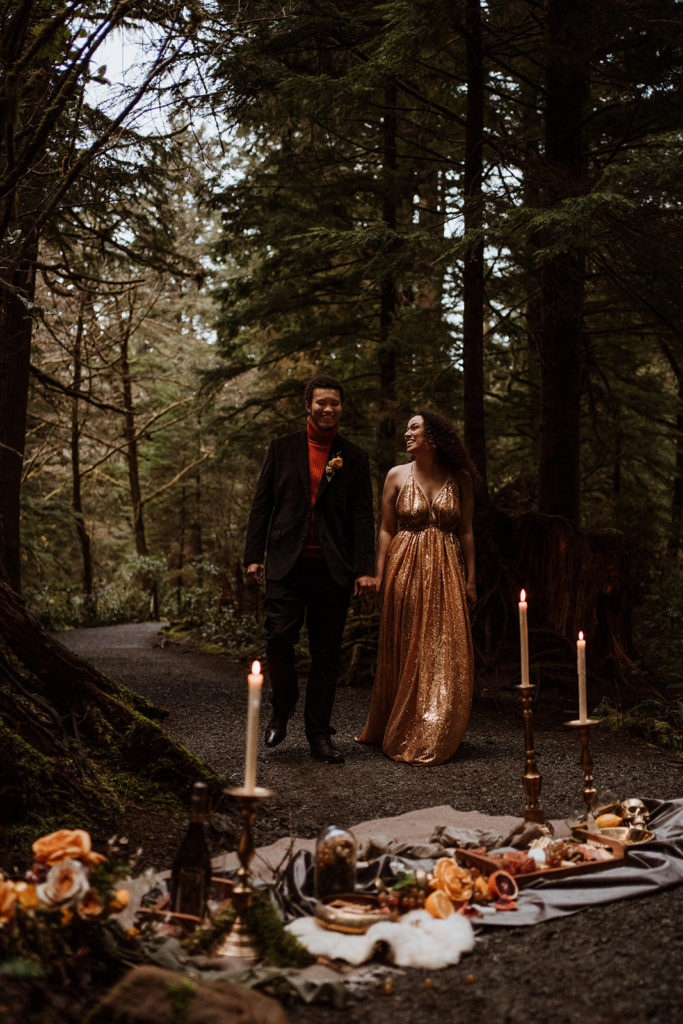 A couple walks holding hands after eloping and looking at one another.  They eloped in the forest on the coast of Oregon.
