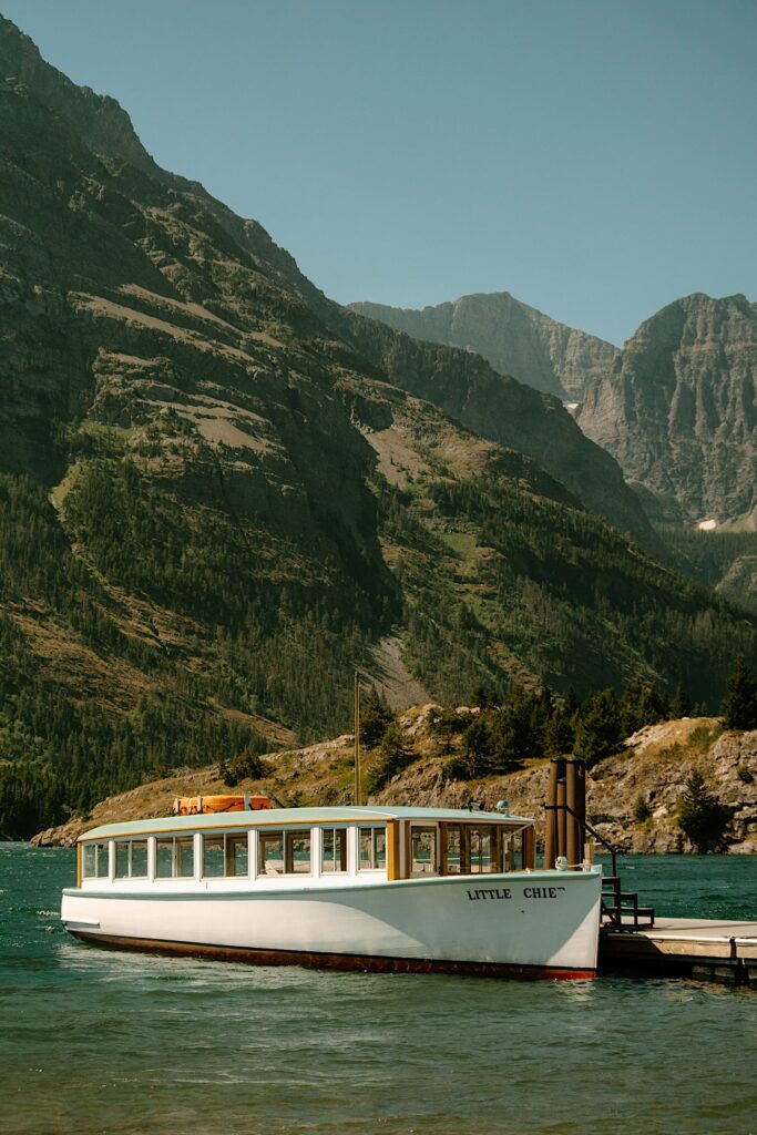 A boat named the Little Chie sits at a pier in front of mountains at Glacier National Park