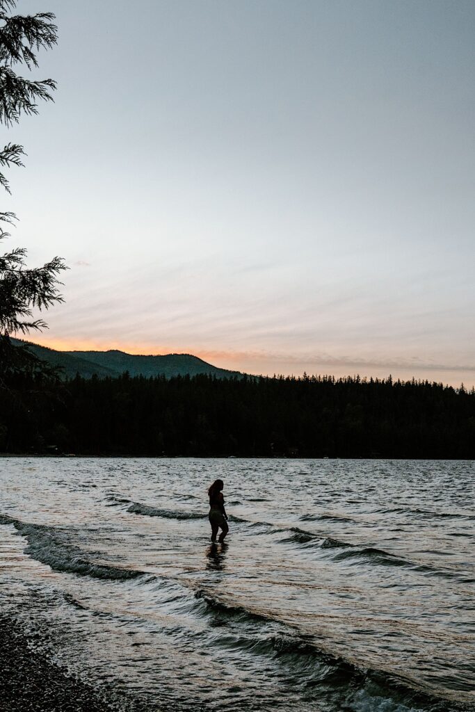 A girl stands looking out over a lake in Glacier National Park in sunset.
