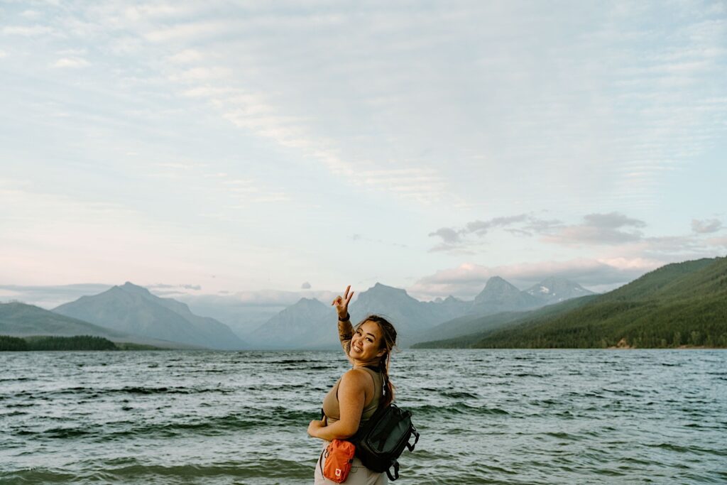 Kriztelle Halili, owner of Kriztelle Halili Photography stands in front of mountains at Glacier National Park looking back at the camera and smiling.