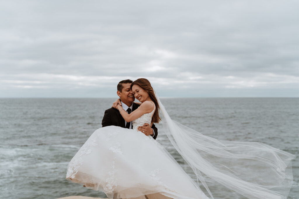 A groom stands holding his bride in Big Sur on the California coast.